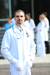 Fototapeta premium Happy doctor with medical stuff behind standing against clinic entrance
