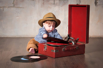 Funny baby boy in retro hat with vinyl record and gramophone