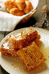 Honeycombs on plate, hot buns in basket on wooden background