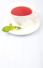 A cup of hibiscus tea and fresh mint leaves over white background