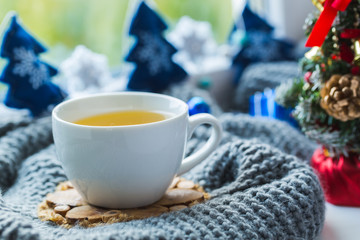 White cup of chamomile tea with grey scarf on the windowsill.
