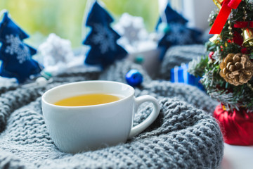White cup of chamomile tea with grey scarf on the windowsill.