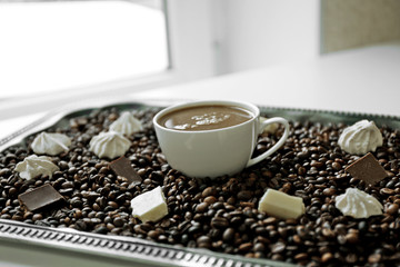 Cup of coffee with sweets and coffee beans on a tray