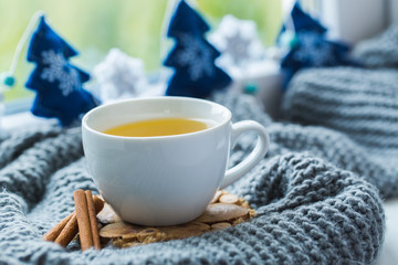 White cup of chamomile tea with grey scarf on the windowsill.