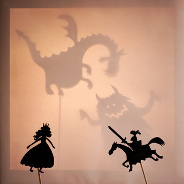 Shadow Puppets of Beautiful Princess and Brave Knight. Bright glowing screen of shadow theatre with monsters shadows in the background.