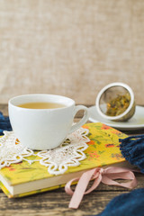 White cup of chamomile tea and book on table.