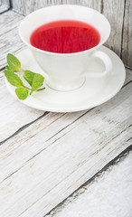 A cup of hibiscus tea and fresh mint leaves over wooden background