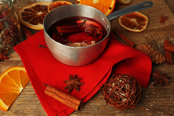 Mulled wine in stew-pan on decorated with red napkin, cinnamon and orange wooden background