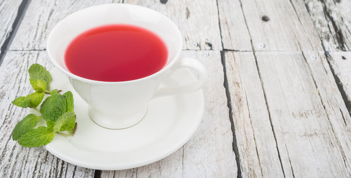 A cup of hibiscus tea and fresh mint leaves over wooden background