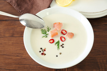 Delicious salmon cream soup with spoon on wooden table, close up