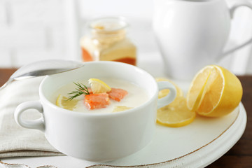 Delicious salmon cream soup with sliced lemon on white tray, close up