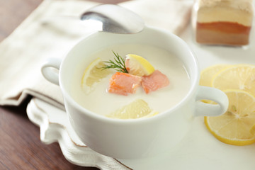 Delicious salmon cream soup with sliced lemon on white tray, close up