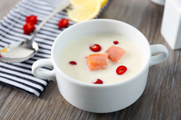 Tasty fish cream soup, lemon, salt and striped cotton serviette on wooden table, close up