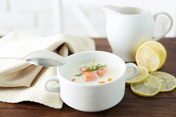 Delicious salmon cream soup with spoon on wooden table, which served with sliced lemon and spices