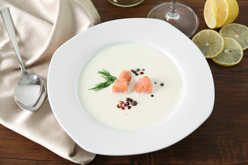 Delicious salmon cream soup with spoon on wooden table, close up