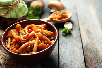 Delicious marinated mushrooms in bowl on wooden background
