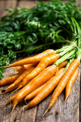 Raw carrot with green leaves on wooden background