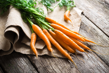 Raw carrot with green leaves on wooden background