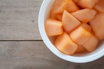 closeup melon slice in white dish with wood table background