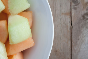 closeup melon slice in white dish with wood table background