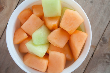 closeup melon slice in white dish with wood table background
