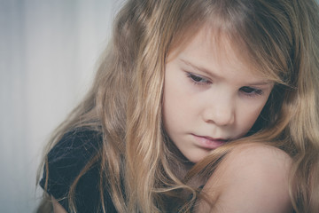 Naklejka premium Portrait of sad little girl sitting near the window