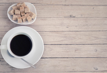 Cup of coffee with brown cube sugar on a wooden table, matte effect.