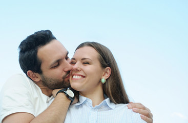 boy kissing his girl's cheek outdoors on blue sky background