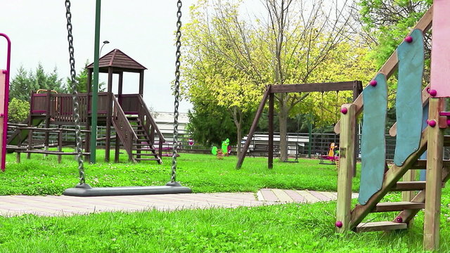 empty swing with chains swaying at playground for child, moved from wind, on green meadow background in slow motion loopable, hd 1080p