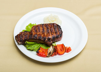 Hot fresh grilled juicy steak on bone with aromatic crust and vegetables on plate (focus on nearest edge of steak)