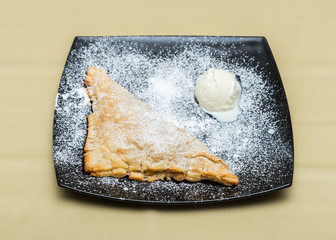 Cake of puff pastry with ice-cream and sugar powder on plate (focus on nearest edge of cake)