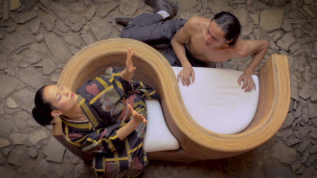 Overhead shot of two traditional butoh dancers - one shirtless - one is blowing kisses to his Japanese partner while she freaks out in fast sharp movements.