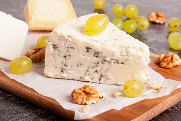 Blue cheese with grapes and nuts on wooden board
