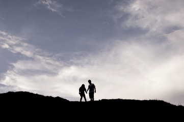 Silhouette of sweet couple holding hands, standing on the mountain
