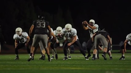 A football is snapped during a game and then thrown toward the camera to a teammate at night - Powered by Adobe