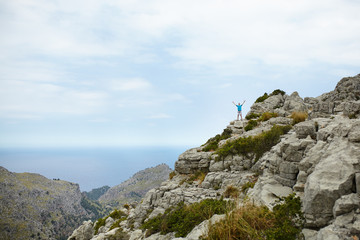 Fototapeta na wymiar Young man standing on cliff with hands raised on top of mountain at Sa Colobra, Majorca, Spain. Happy man winner on top of mountain.