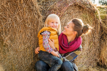 Portrait of woman and happy child sitting on hay on farm © Alliance