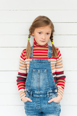 Fashion portrait of a cute little girl against white background, wearing stripe roll neck pullover and denim overalls