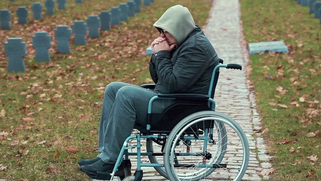 Lonely Disabled veteran in wheelchair at cemetery in autumn