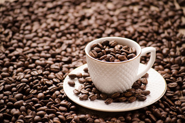 White cup with a saucer on grains of coffee on a table