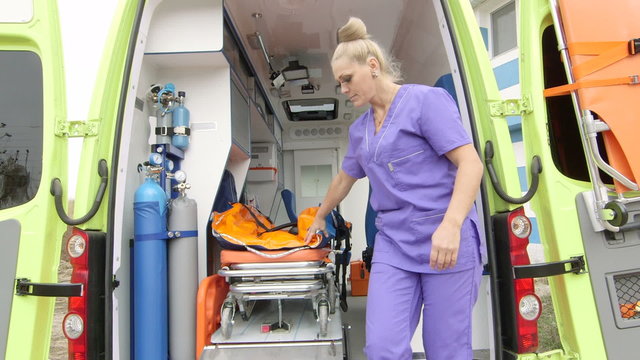 Emergency medical service female paramedic taking stretcher out of an ambulance at the site of illness or injury