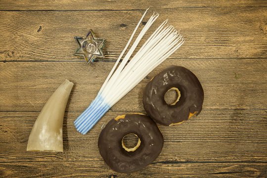 Donuts goat horn candles and star of David Hanukkah symbols on wooden background.