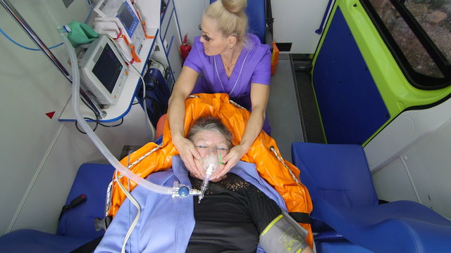 Emergency medical service paramedic holding patient head wearing oxygen mask in ambulance monitoring obese senior woman condition during transportation to the nearest hospital