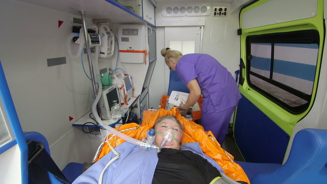 EMT paramedic provide medical care to critical senior patient wearing oxygen mask in ambulance using life support kit, woman  with eyes closed lying on stretcher