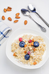 Oatmeal porridge with berries and nuts in bowl, top view