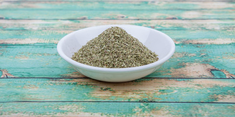 Dried oregano herbs in white bowl over wooden background