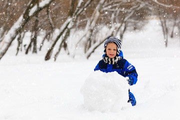 Fototapeta na wymiar cute little boy building snowman in winter