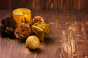 X-mas greeting card: golden candle, pine cones and christmas decorations over old brown wooden background. Selective focus. Vintage style