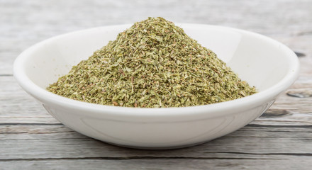 Dried oregano herbs in white bowl over wooden background