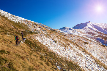 Fototapeta na wymiar Winter Mountain Range View and Group of Trekkers Walking Up on Trail Shining Sun on Clear Sky